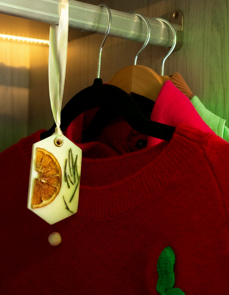Red sweater with a wax sachet featuring orange slices of lemon and rosemary, hanging on a rack.