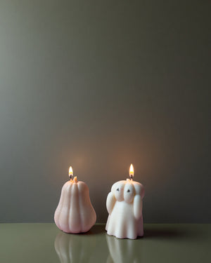 Two soy wax candles shaped like a pumpkin and a ghost on a reflective surface with a dark background