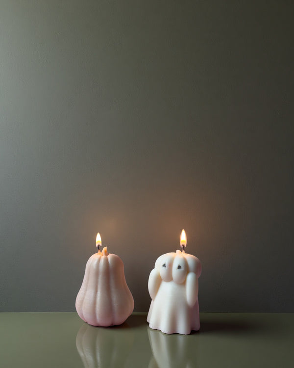 Two soy wax candles shaped like a pumpkin and a ghost on a reflective surface with a dark background