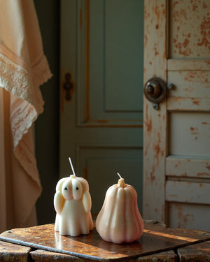 Two decorative candles shaped like a ghost and a pumpkin from lila with love on a rustic wooden surface with a vintage door in the background.