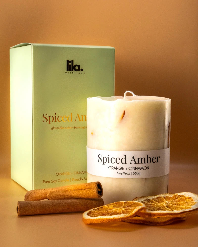 Spiced Amber from lila with love candle with packaging and with cinnamon stick and dried lemon slices  on a warm background