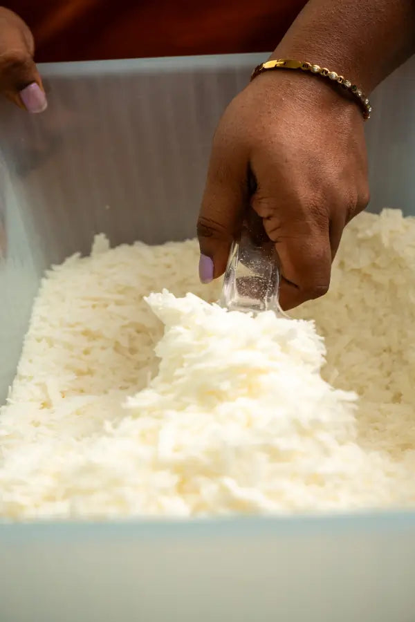 Person's hand scooping white soy wax from a container