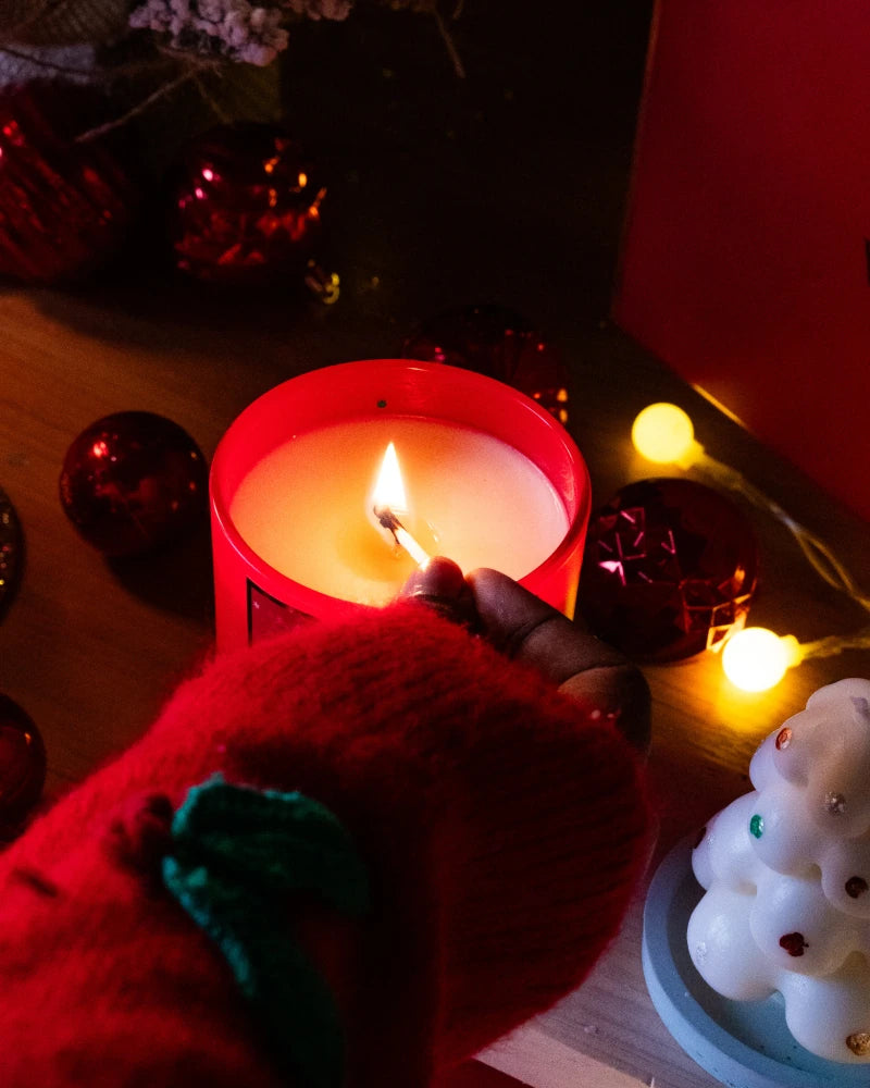 Hand lighting a red jar candle from lila with love with festive decorations in the background