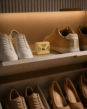 A yellow lila with love scented wax pod on a lit wardrobe shoe shelf between white and tan sneakers, with heels on the shelf below