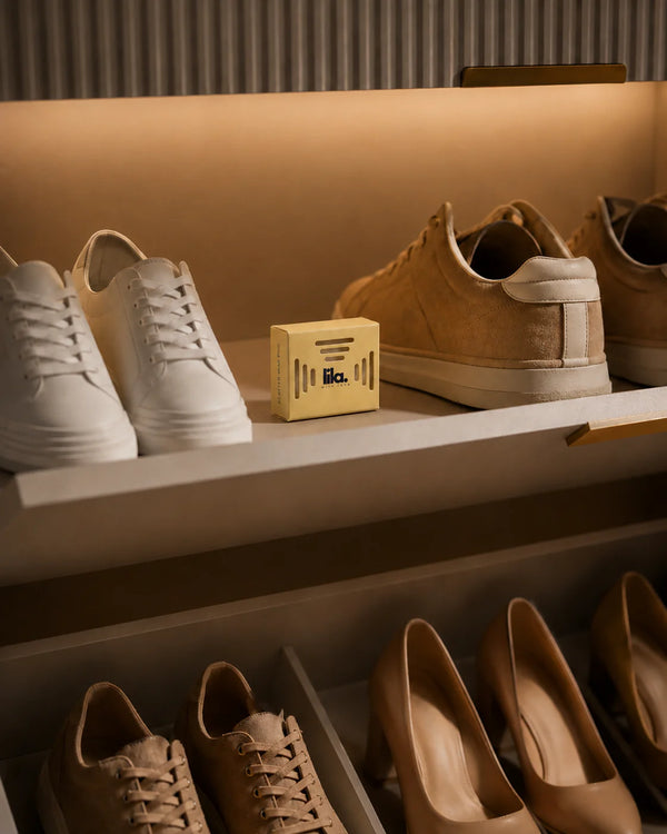 A yellow lila with love scented wax pod on a lit wardrobe shoe shelf between white and tan sneakers, with heels on the shelf below