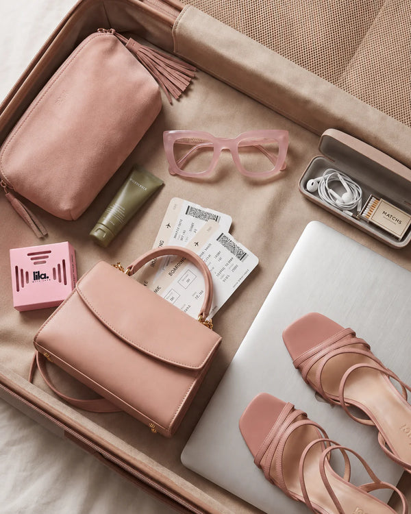 A pink lila with love pod packed in an open suitcase with a handbag, boarding passes, sunglasses, laptop and pink sandals