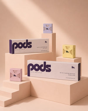 lila with love pods packaging on blush plinths — two "set of 4 scented wax pods" boxes with individual lilac, yellow and pink pods