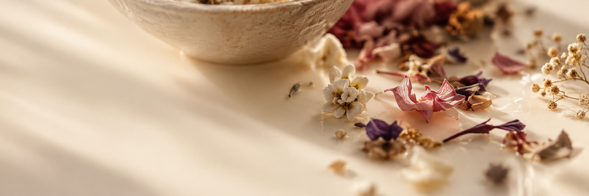 Dried flowers and petals scattered beside a stone bowl in soft sunlight