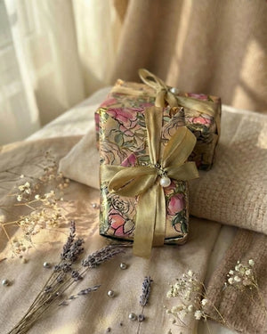 Gift box with floral wrapping and gold ribbon on a textured surface with dried flowers.
