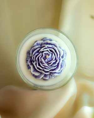 Dusky blue layered flower soy wax candle in clear glass jar by Lila with Love, top view on satin background
