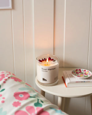Handcrafted rose soy candle by lila with love on a round table, styled with a floral throw and open book — a romantic home fragrance scene.