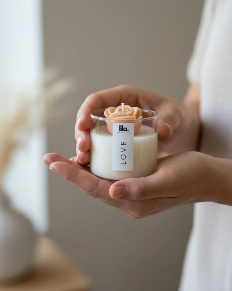 Hand holding a small candle labeled 'LOVE' from lila with love with a blurred background
